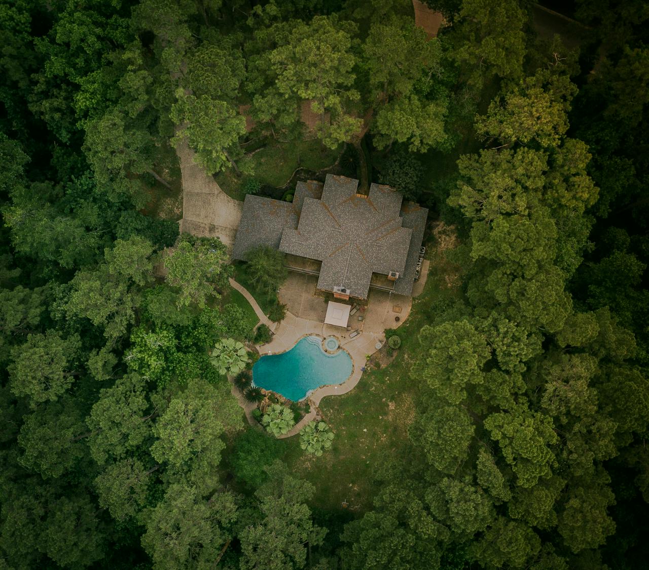 gallery-4 A scenic aerial shot of a house surrounded by lush forest and a swimming pool.